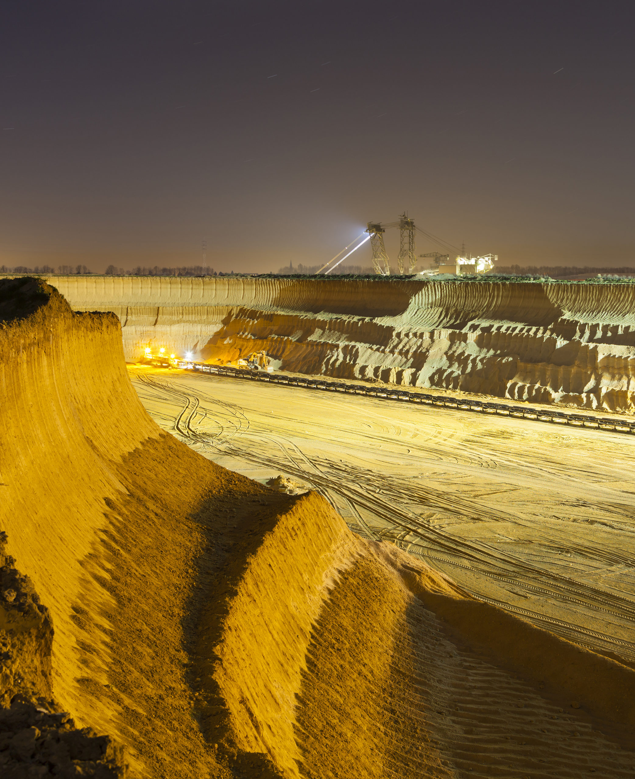 Pit Mine Wall At Night - A steep lignite pit mine wall illuminated at night with an excavator in the background