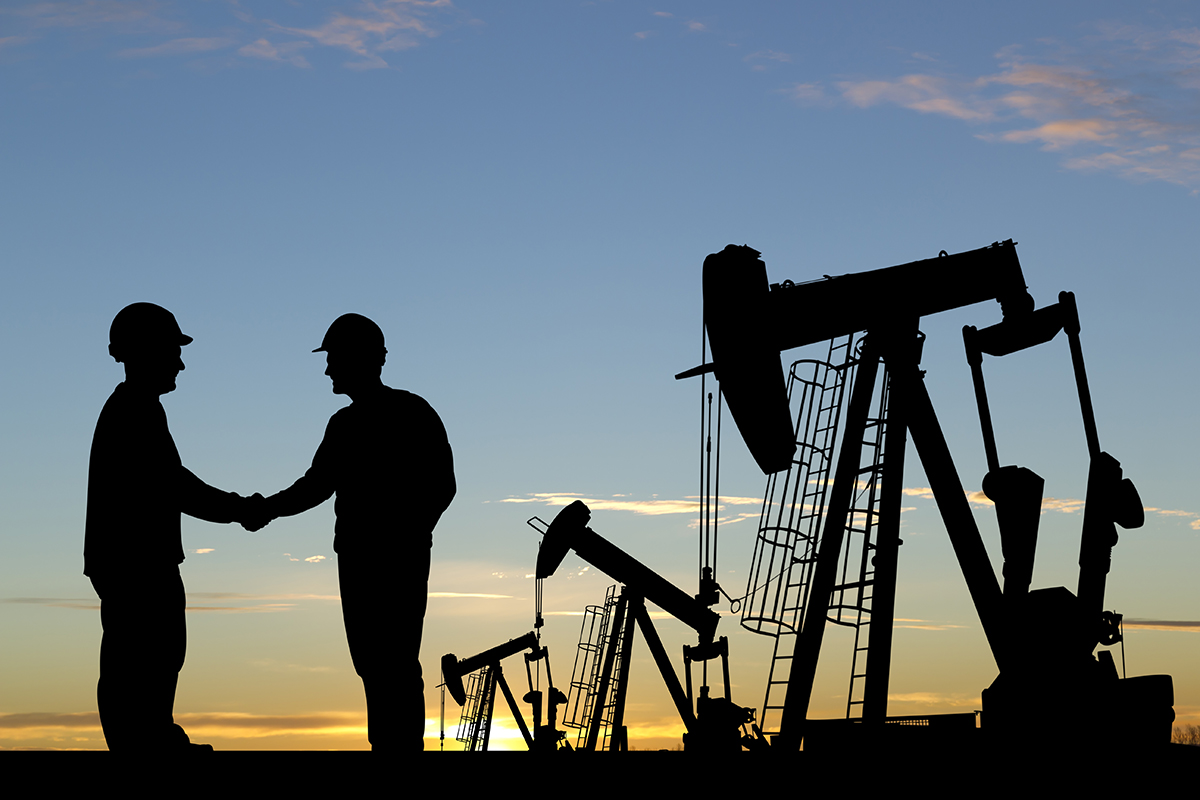 A royalty free image from the oil and gas industry of two oil workers shaking hands in an oil field.